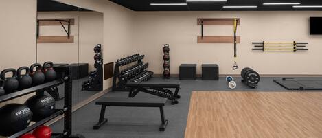 A gym with kettlebells, dumbbells, a bench, and a pull-up bar.