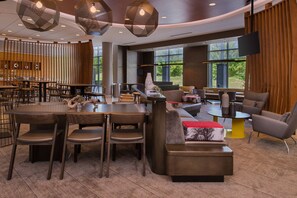 A modern dining area with a round table, chairs, and a sofa. There are large windows providing natural light and a view of the outdoors. - SpringHill Suites by Marriott Pittsburgh Southside Works (Pittsburgh)