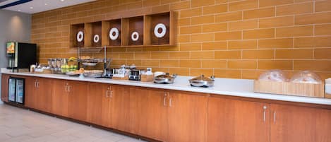 A buffet area with a long counter, wooden cabinets, and various food items.