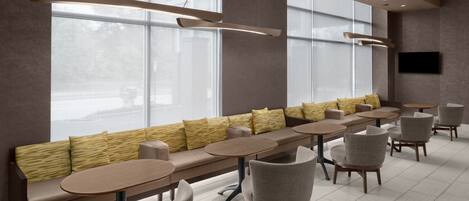 A modern cafe with a long bench, round tables, and chairs.
