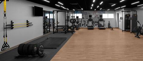 Un gimnasio con equipo de levantamiento de pesas, cintas de correr y bicicletas estáticas.