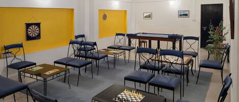 A room with a dartboard, chessboard, and multiple tables and chairs.