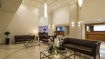 A spacious lobby with a high ceiling, two sofas, a reception desk, and a staircase.