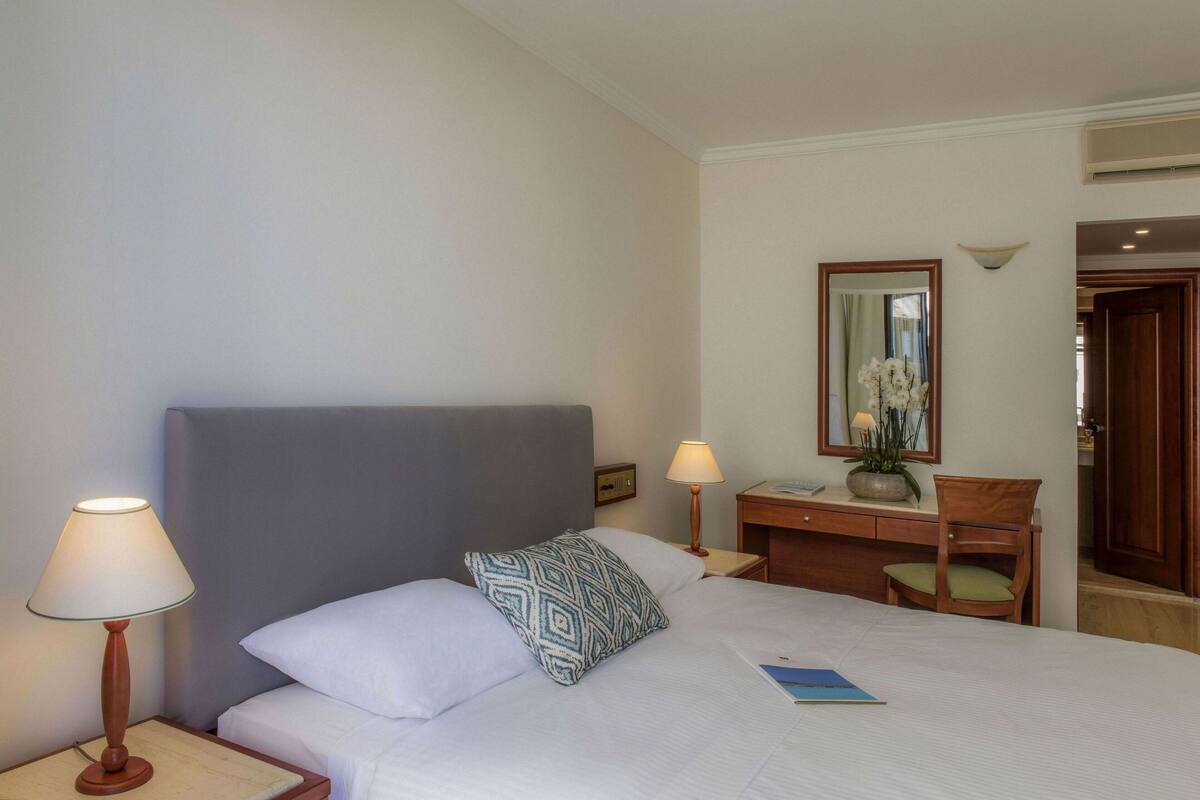 Een hotelkamer met een bed, twee bedlampjes, een dressoir, een spiegel en een stoel.