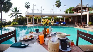 Una mesa de comedor junto a una piscina, con alimentos para el desayuno, bebidas y un florero.