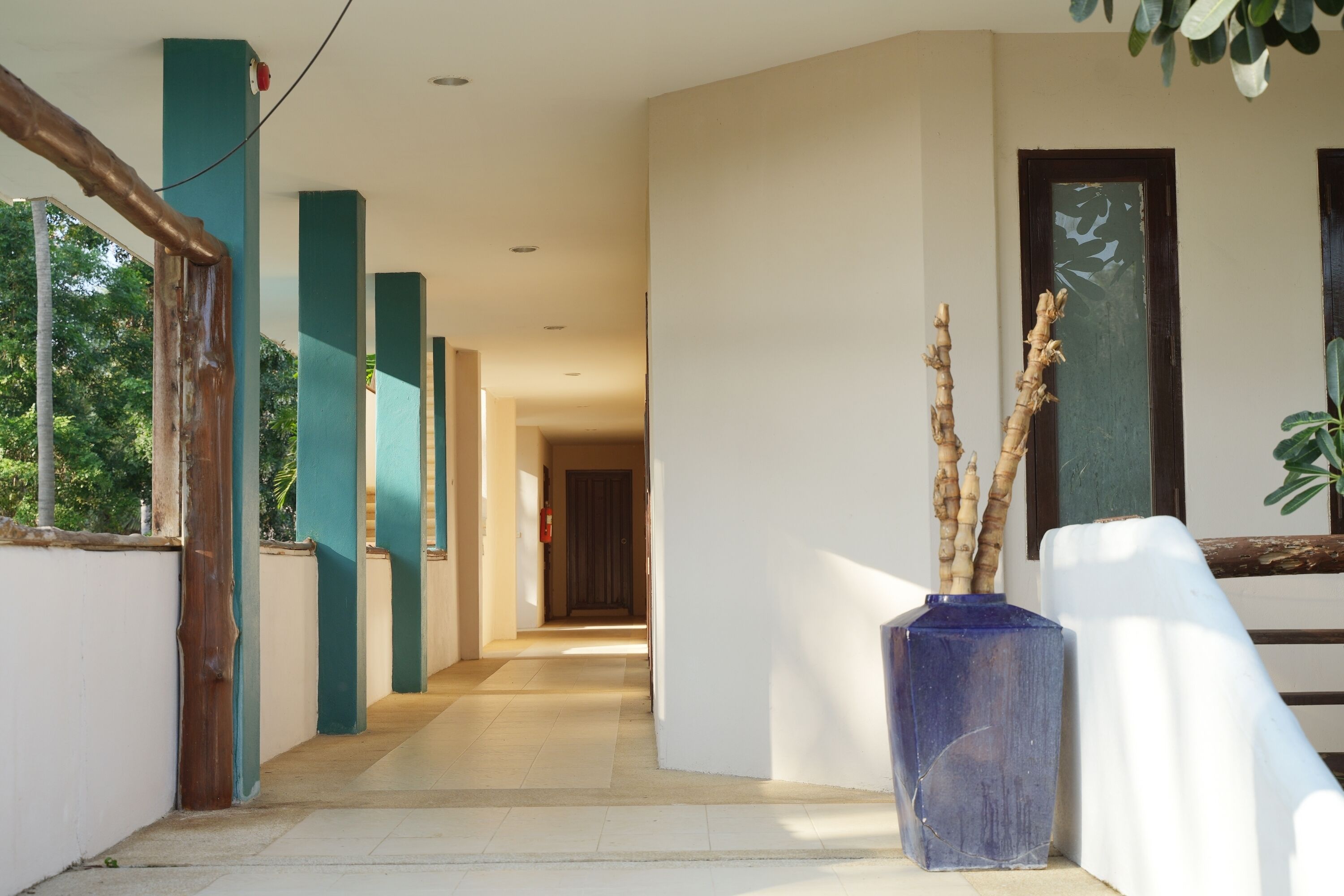 A corridor with teal pillars, a blue vase with branches, and a door with a window.