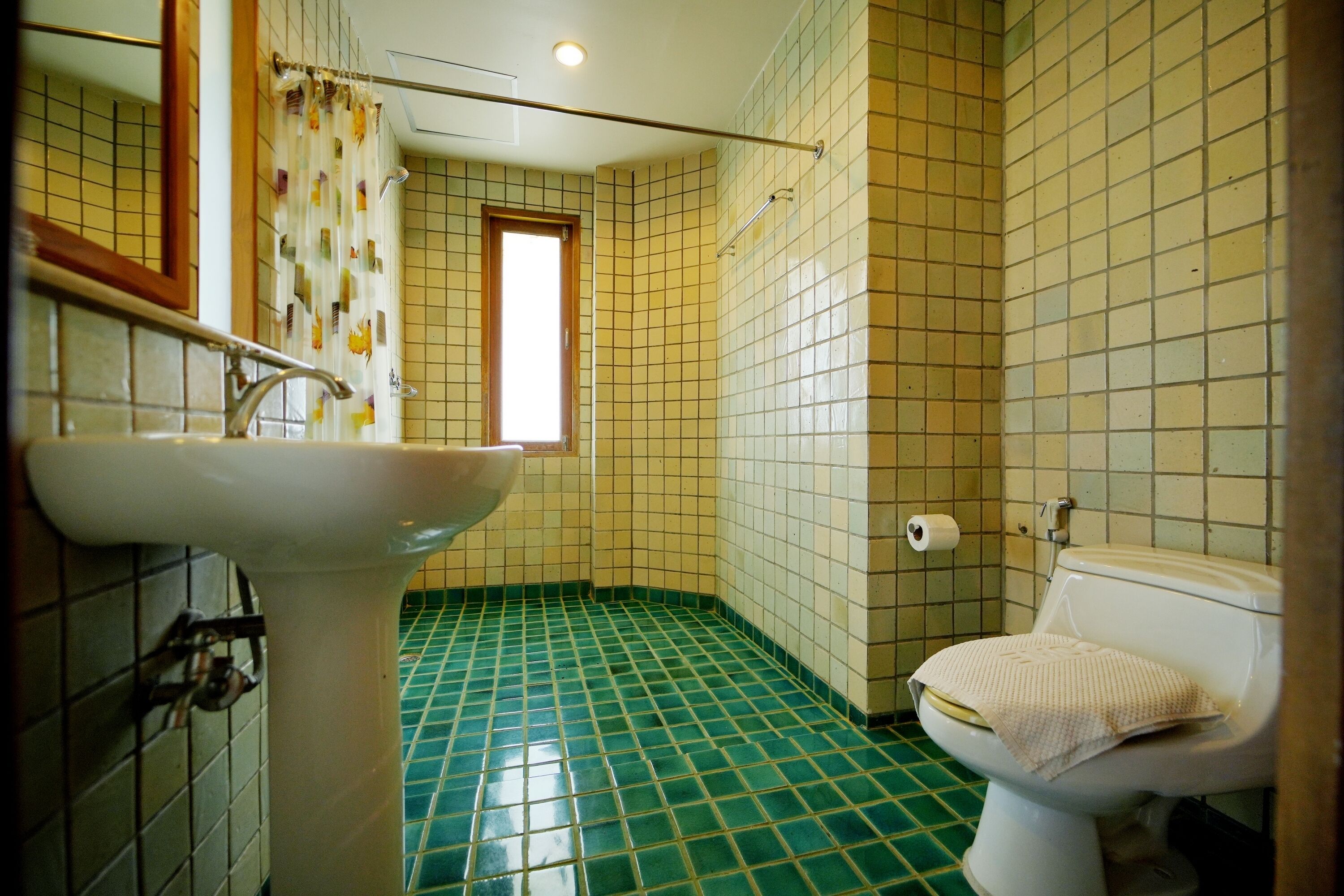 A bathroom with a green-tiled floor, a white sink, and a toilet with a towel on it.