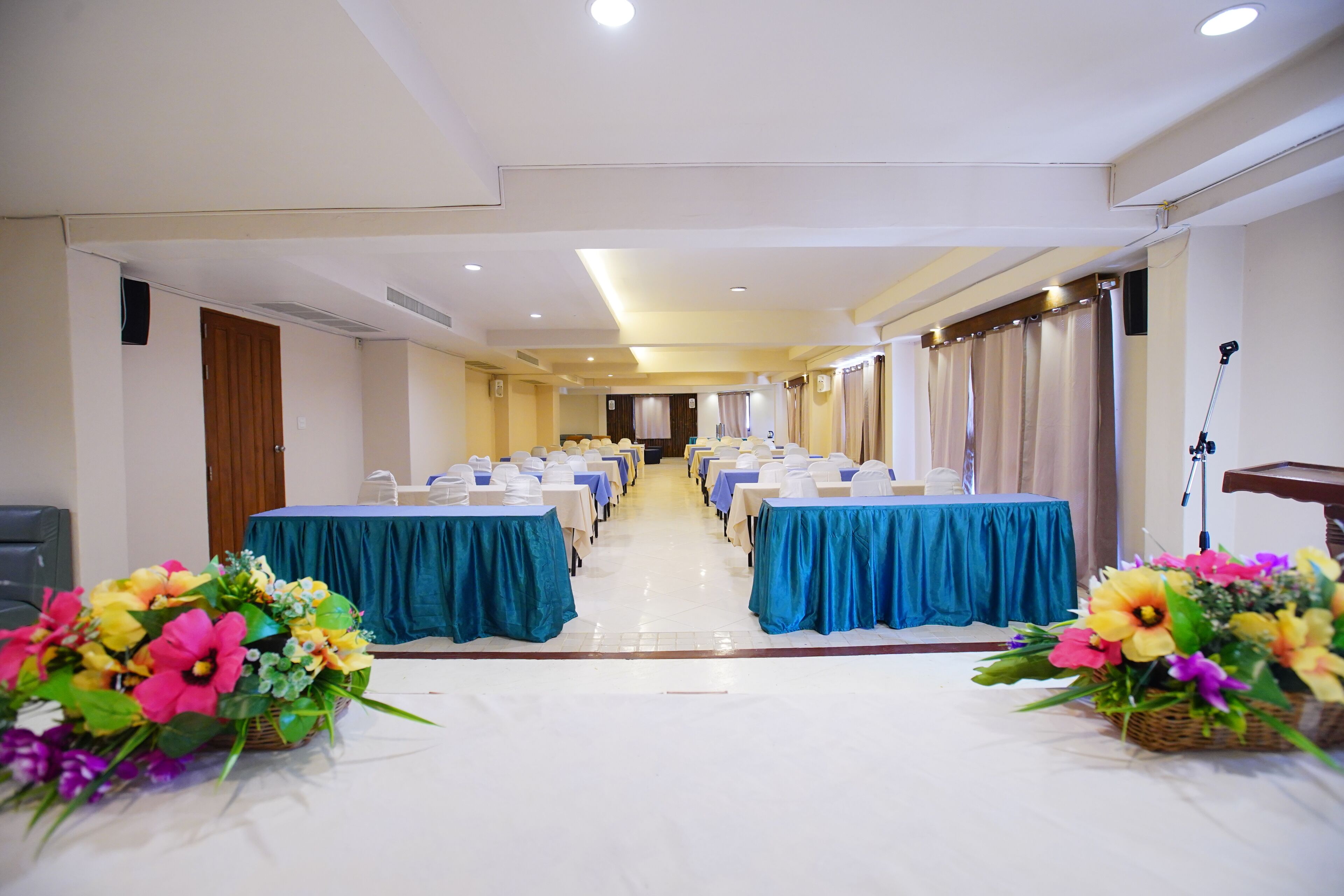 A conference room with rows of tables, blue tablecloths, and floral centerpieces.