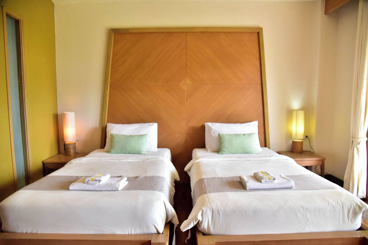 Ein Hotelzimmer mit zwei Betten, jeweils mit weißer Bettwäsche und grünen Kissen, sowie einem Holzkopfende.