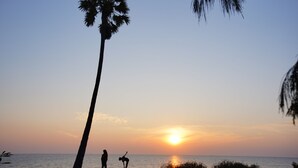 Escena de playa con un atardecer, palmeras y siluetas de personas.