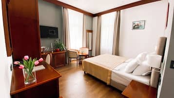 Habitación de hotel con cama, mesita de noche, escritorio, silla y una pequeña mesa con una planta.