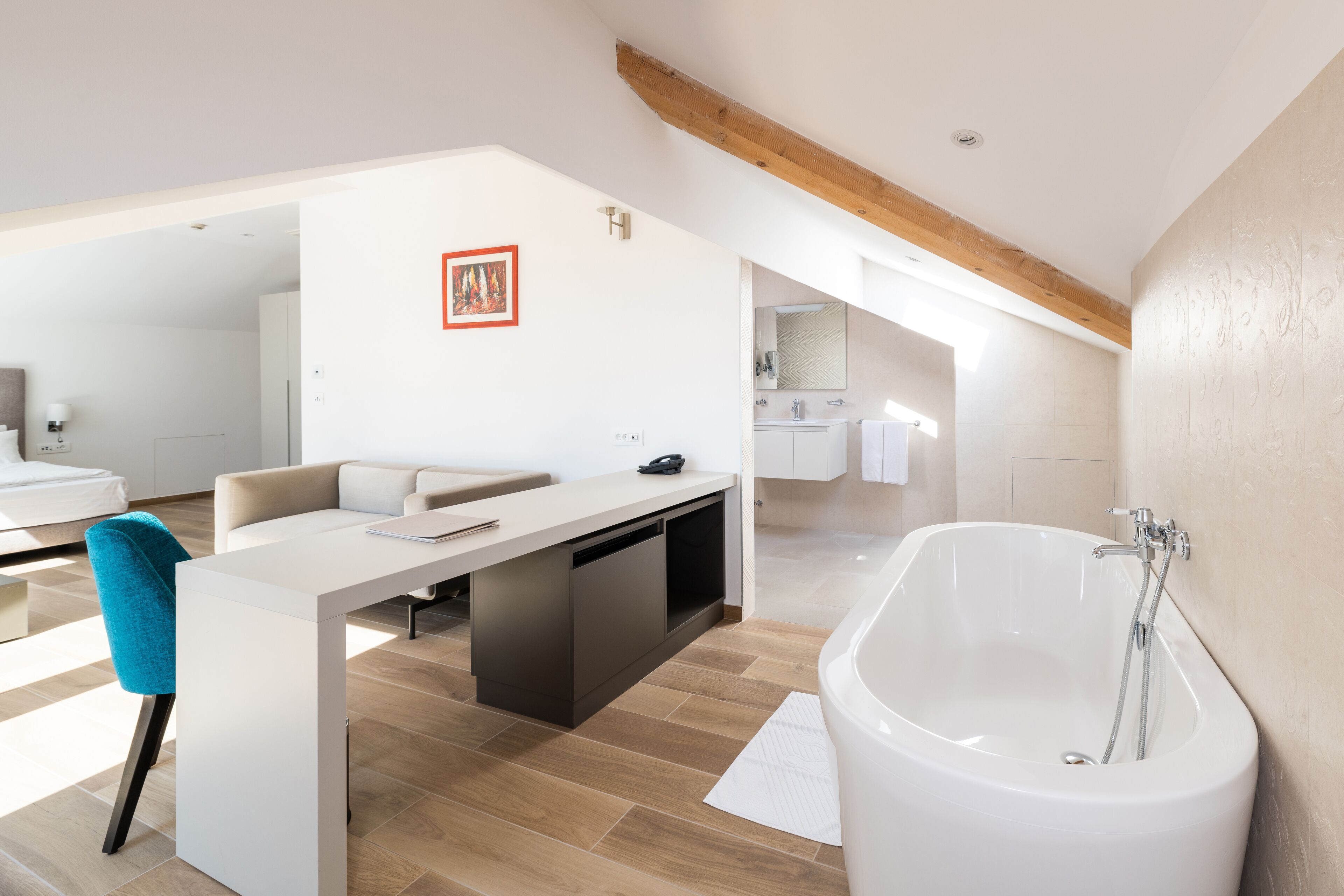 Quarto de hotel moderno com uma banheira grande, área de jantar com mesa e cadeiras, e sala de estar separada com um sofá.