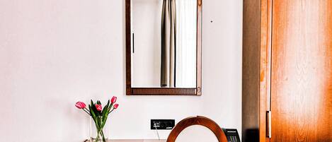 Un bureau en bois avec un miroir, une chaise, un vase de fleurs et un téléphone.