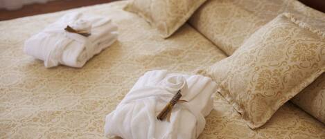A neatly made bed with a patterned bedspread and two pillows, each with a folded white towel and a small decorative item.