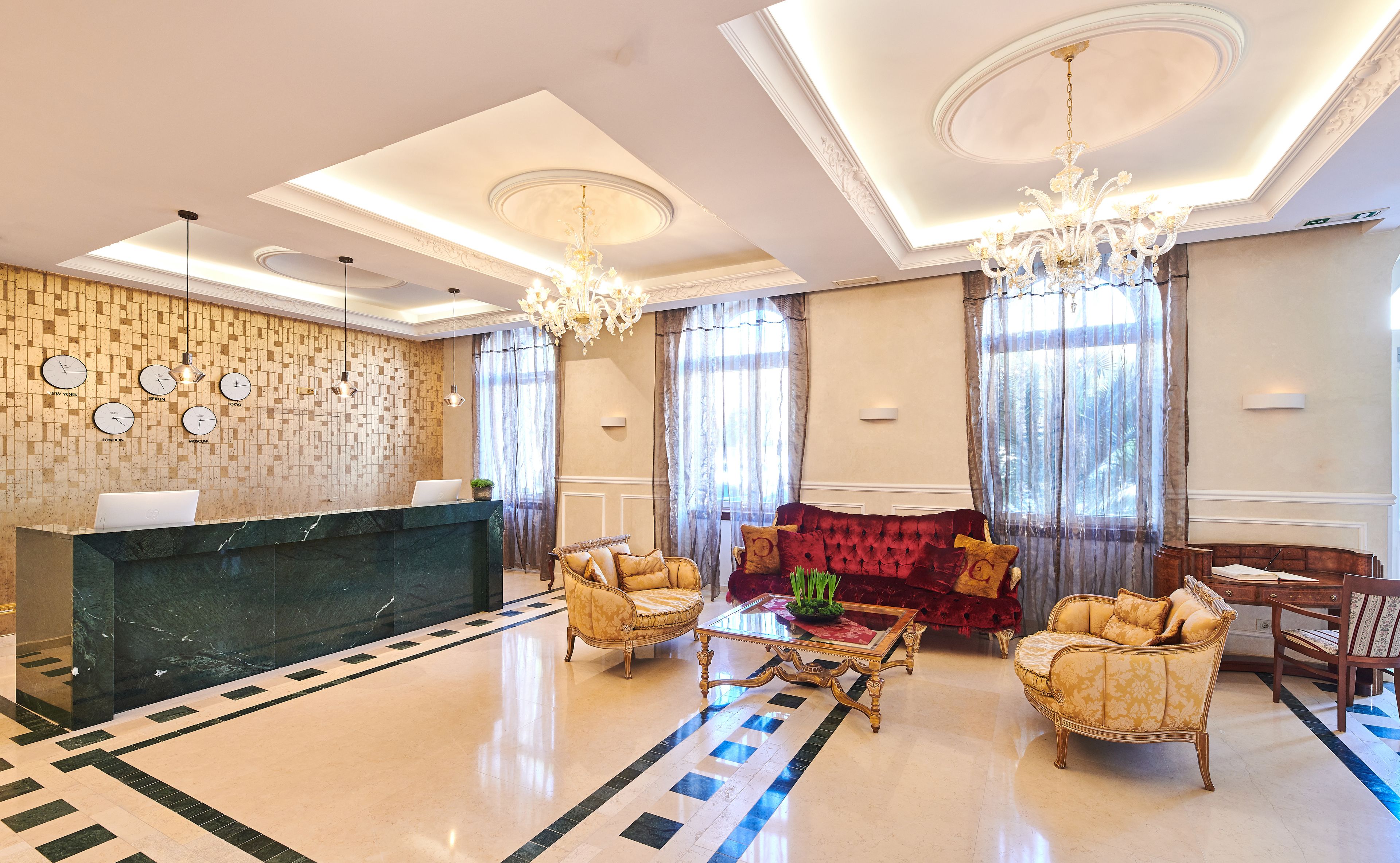 A hotel lobby with a reception desk, seating area, and decorative elements like clocks and a chandelier.