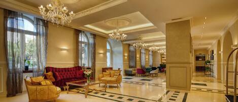 A spacious lobby with a grand chandelier, plush seating, and a marble floor.