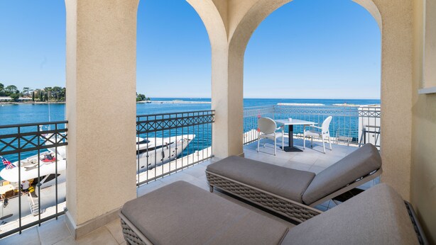 Een balkon met uitzicht op zee, met een zithoek met twee comfortabele stoelen en een bijzettafeltje.