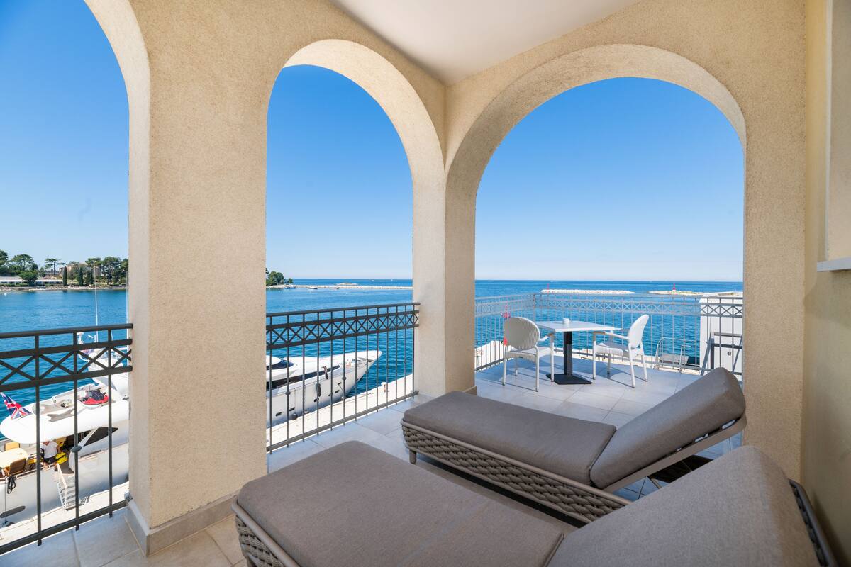 A balcony with a view of the sea, featuring a lounge area with two cushioned chairs and a small table.