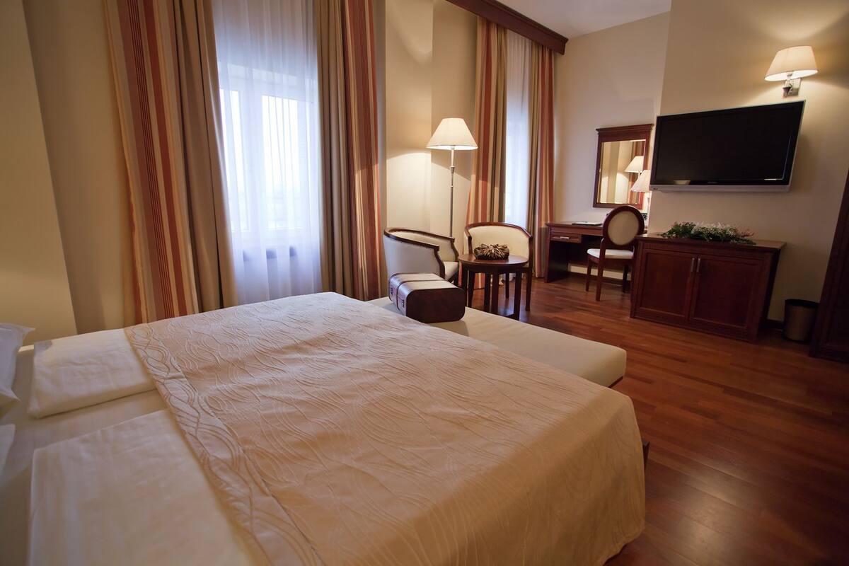 A hotel room with a large bed, a desk, a chair, a television, and a cabinet.