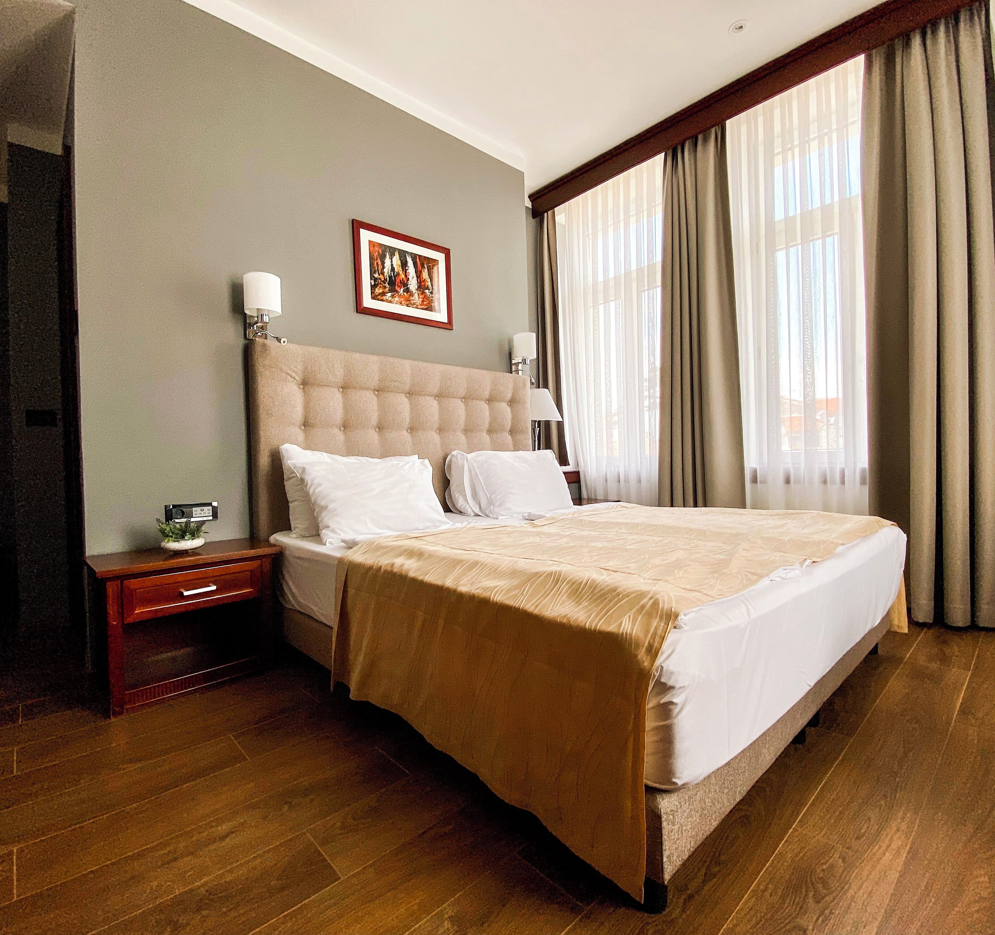 Une chambre d’hôtel avec un grand lit, une table de chevet, un tableau encadré au mur et une fenêtre avec des rideaux.