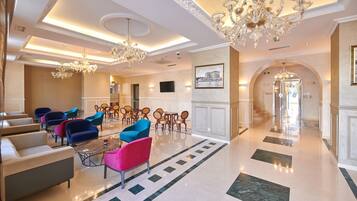 Un'ampia hall con soffitto alto, lampadari e diverse zone relax con divani e poltrone.