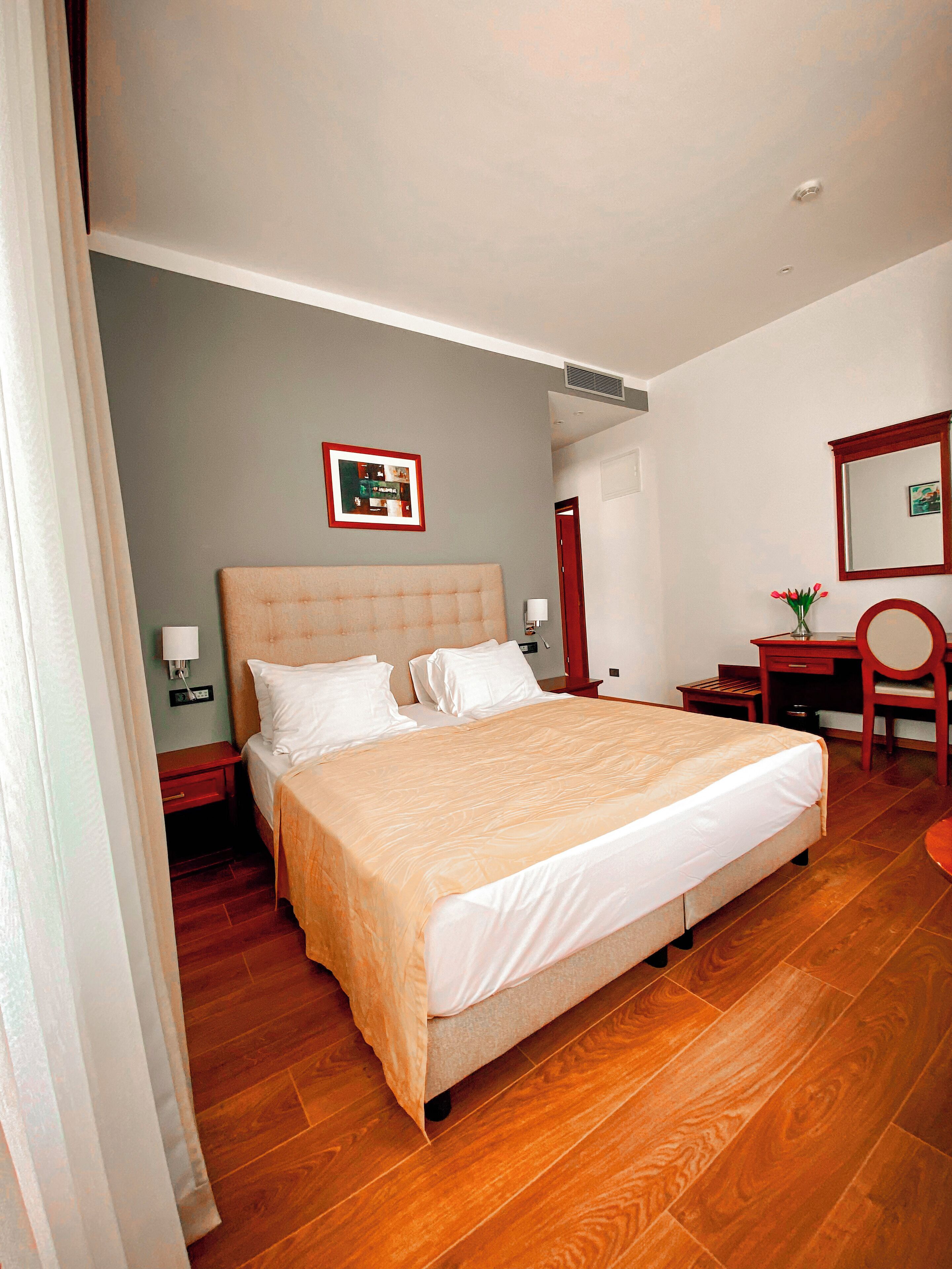 A hotel room with a large bed, a desk, a chair, a mirror, and a picture on the wall.