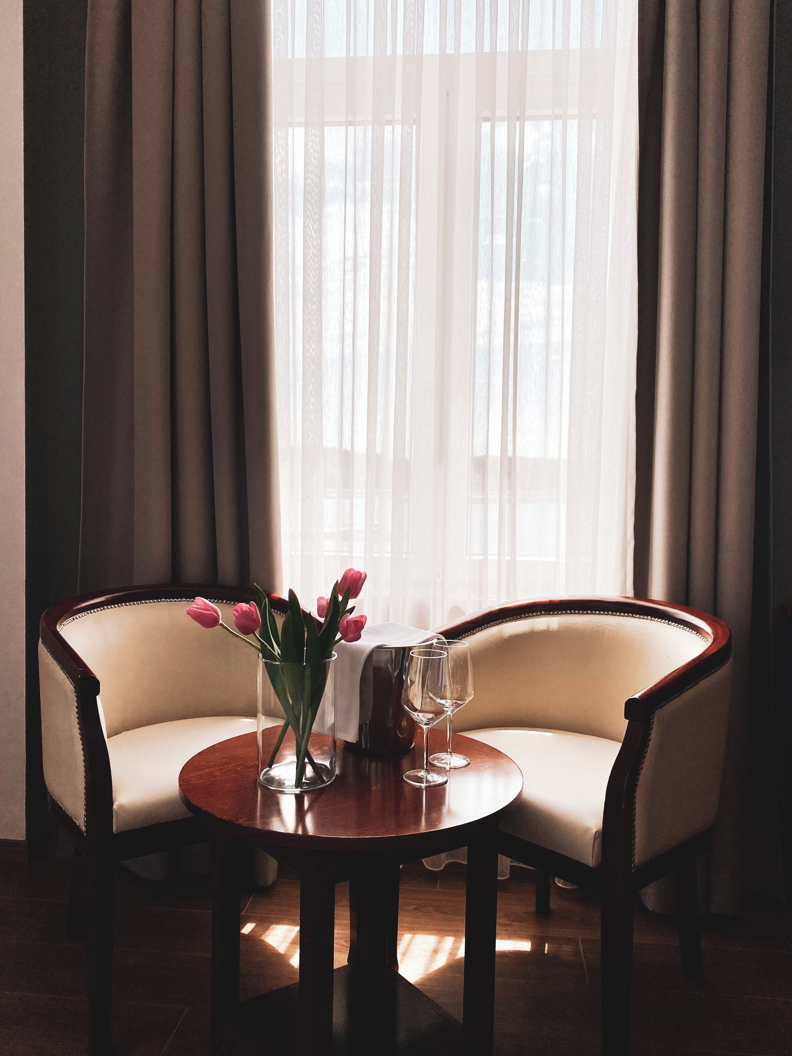 A room with a round table, two chairs, a vase with flowers, and a glass pitcher.