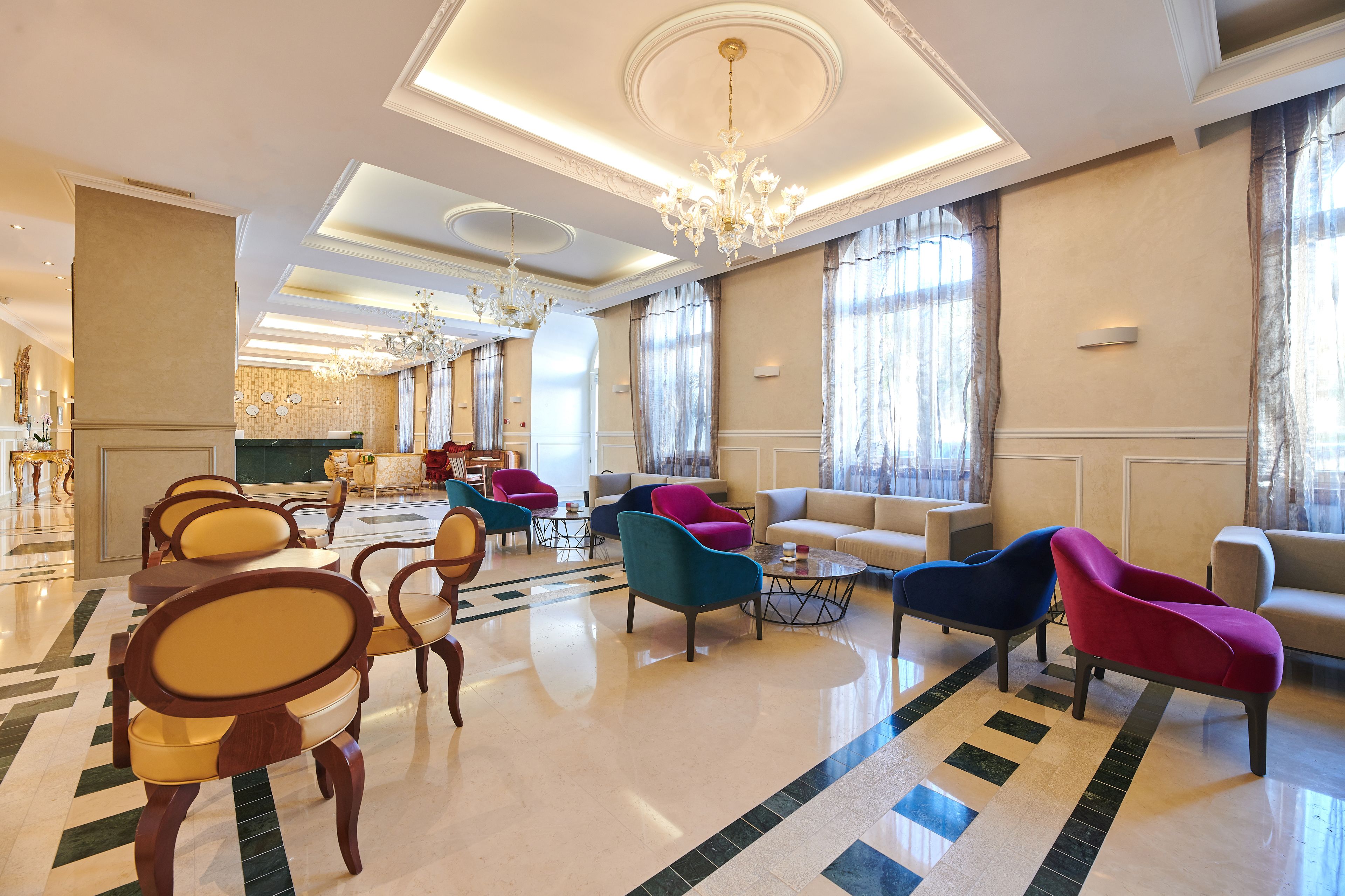 Un vestíbulo amplio con un piso de mármol pulido, candelabros elegantes y diversas opciones de asientos, incluyendo sillones y sofás.