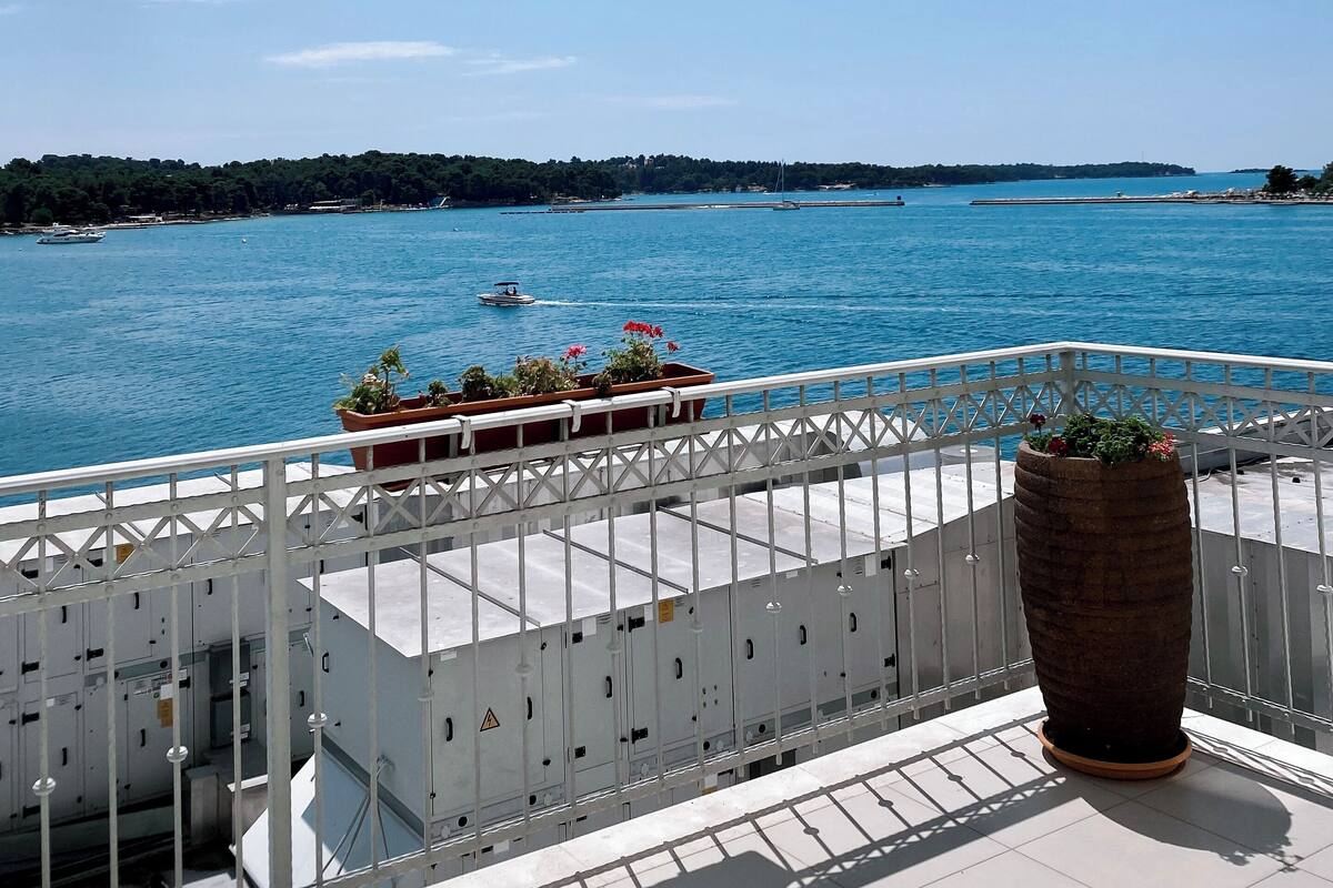 A balcony with a view of a calm sea, potted plants, and a railing.