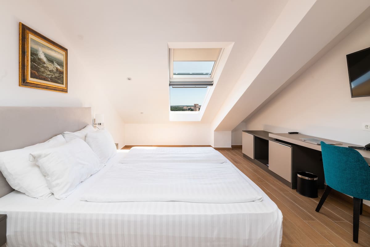 A bedroom with a large bed, a desk, and a skylight.
