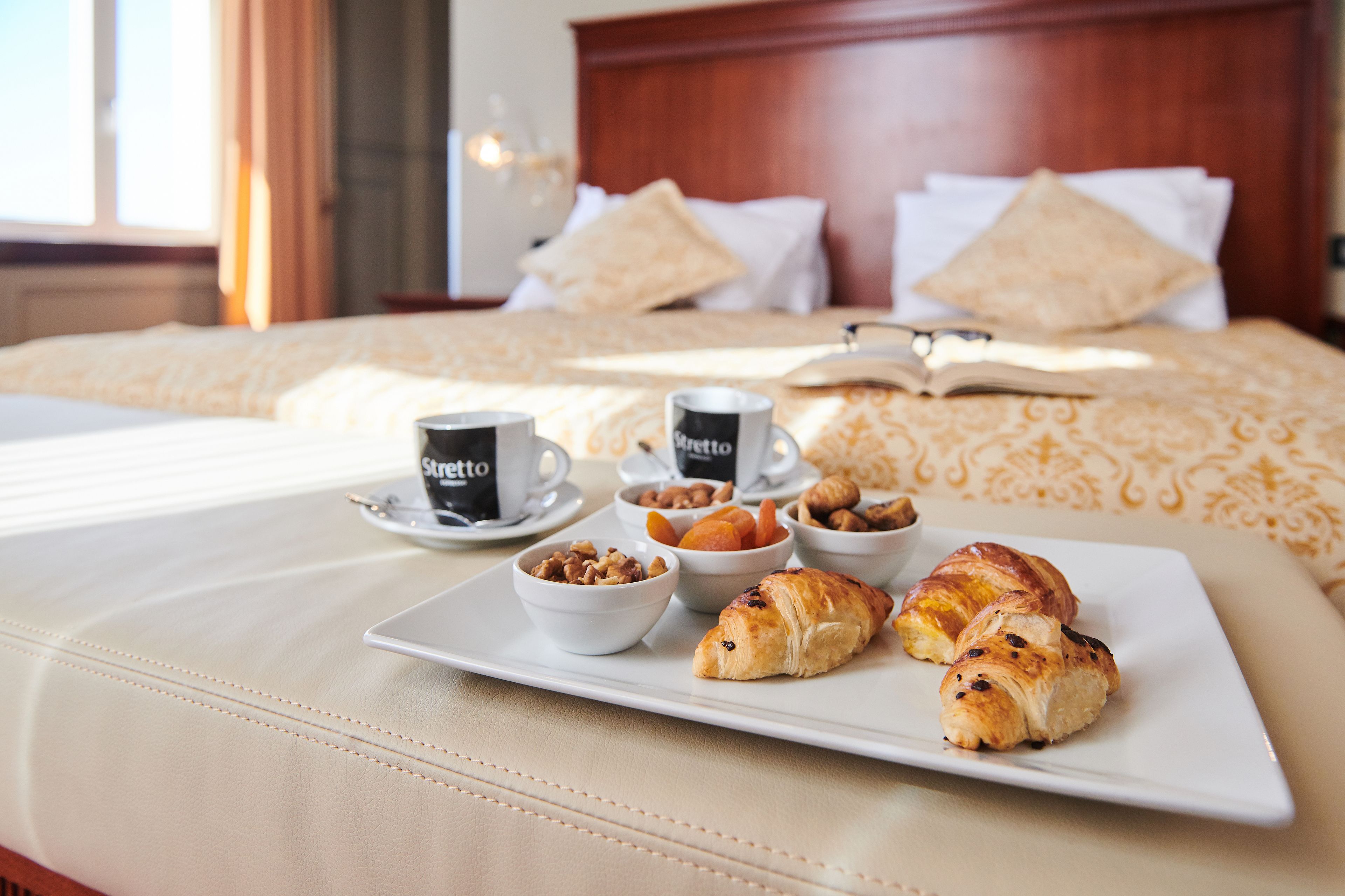 A neatly made breakfast tray with croissants, nuts, and coffee on a hotel bed.