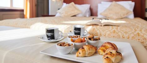 A neatly made breakfast tray with croissants, nuts, and coffee on a hotel bed.