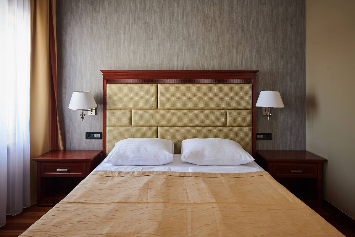 A hotel room with a large bed, two bedside tables, a headboard, and two wall-mounted lamps.