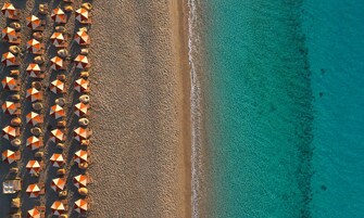 Vista aérea de una playa con hileras de sombrillas y un mar azul cristalino.