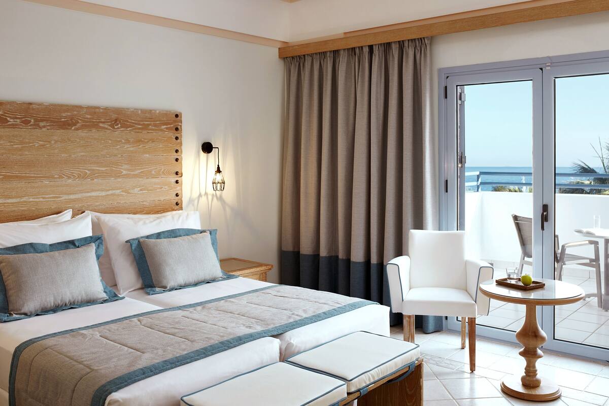A hotel room with a bed, a chair, a table, and a view of the sea.