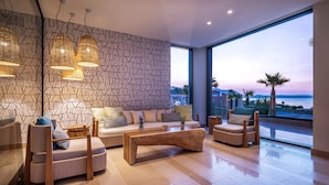 A modern living room with a large window, a patterned wall, and a wooden coffee table. - Mitsis Rodos Village (Rhodes)
