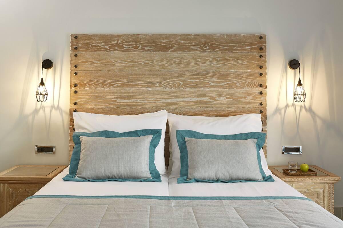 A neatly made bed with a wooden headboard, two bedside tables with lamps, and a small tray with an apple and glass on one of the tables.