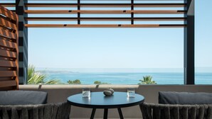 A balcony with a view of the ocean, two chairs, and a round table with glasses and a fruit bowl. - Mitsis Rodos Village (Rhodes)