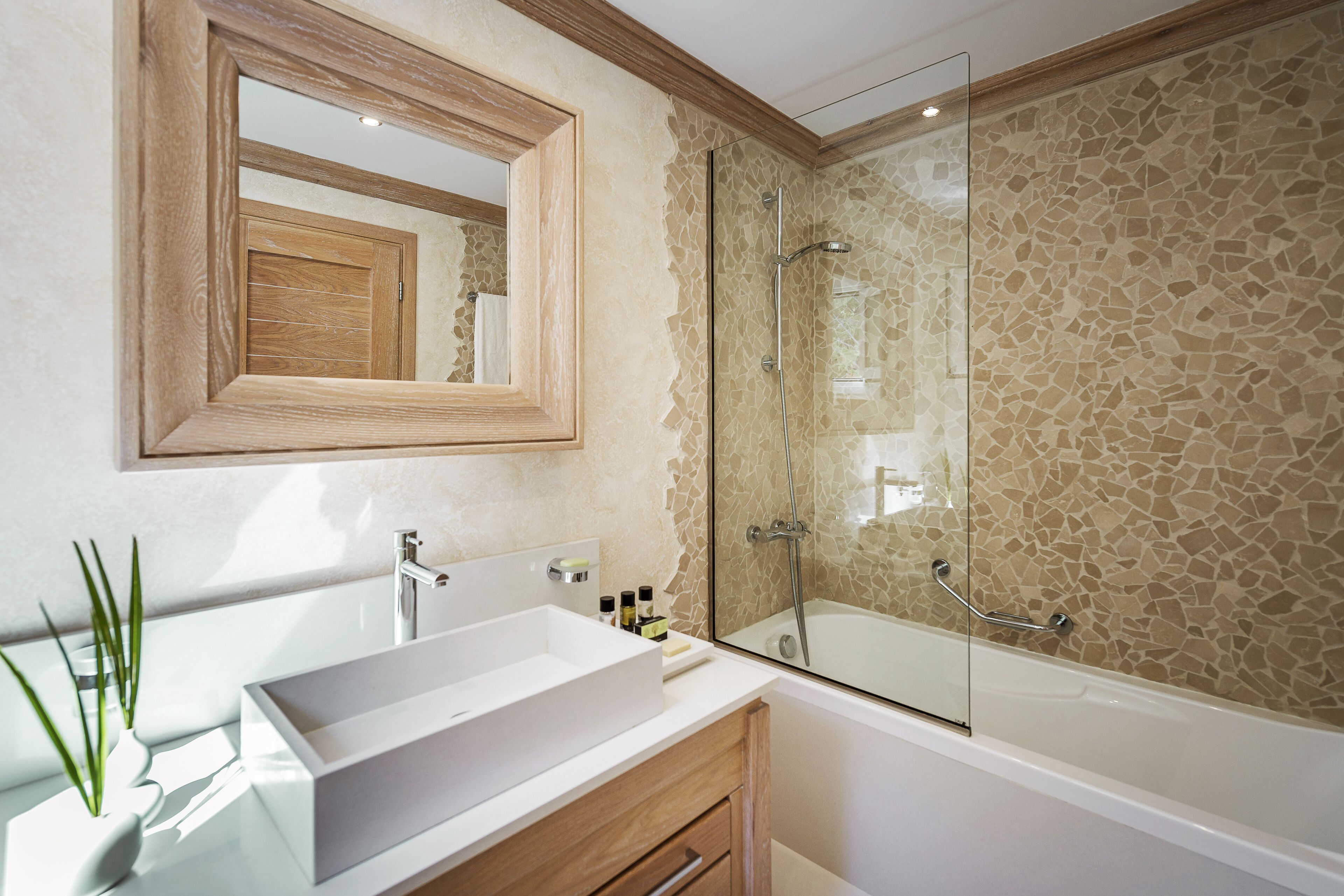 Une salle de bain moderne avec un grand miroir, un lavabo blanc, une douche en verre et un mur orné d’un motif en mosaïque.