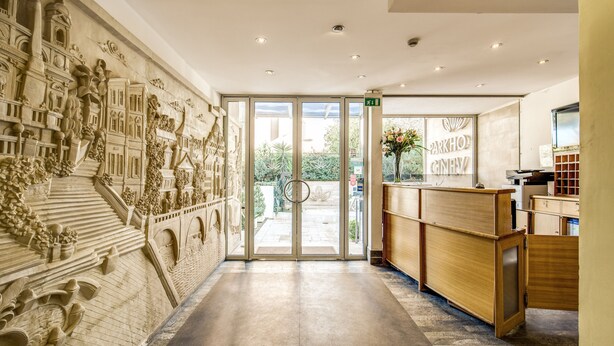 Un área de recepción con un mural detallado en la pared, una mesa de recepción y una puerta de vidrio que da al exterior.