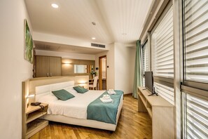 Moderni hotellihuone, jossa on suuri sänky, yöpöydät, työpöytä ja televisio.