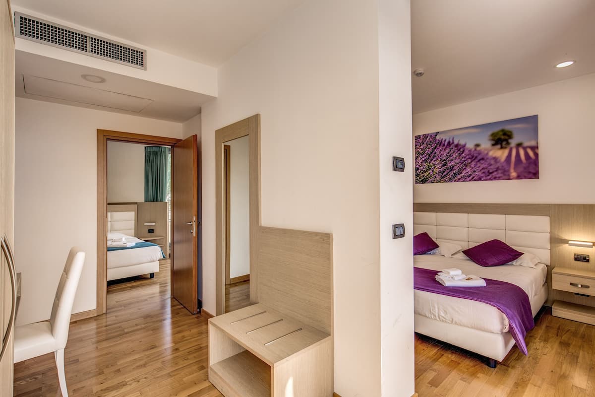 Una camera d'albergo moderna con pavimento in legno, un letto con poggiatesta, un comodino e un quadro appeso al muro.