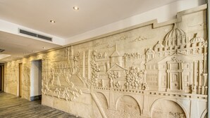 Un pasillo con un elaborado mural de mármol que representa escenas arquitectónicas, un piso estampado y una rejilla en el techo.