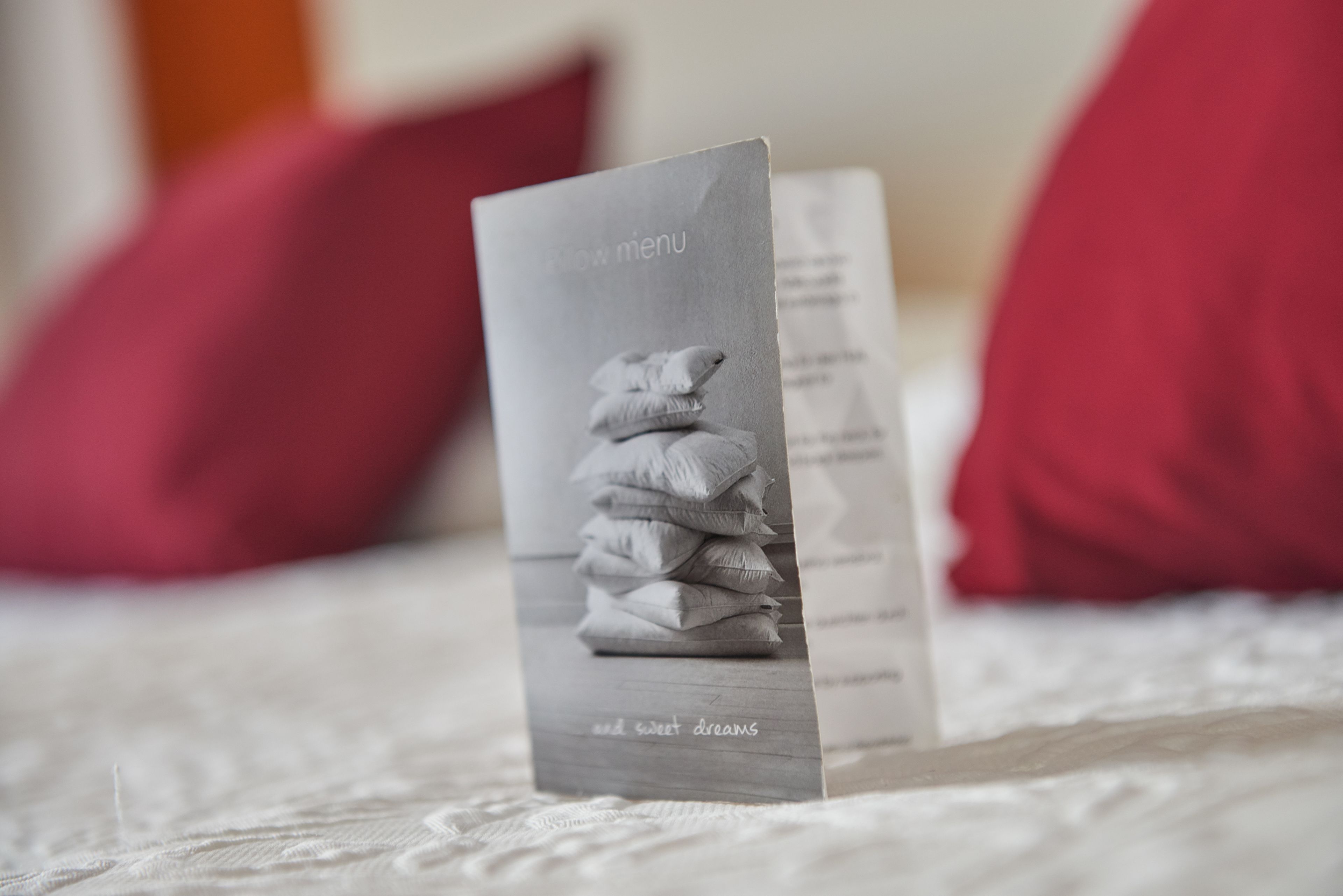 A stack of pillows with a menu card on a bed.