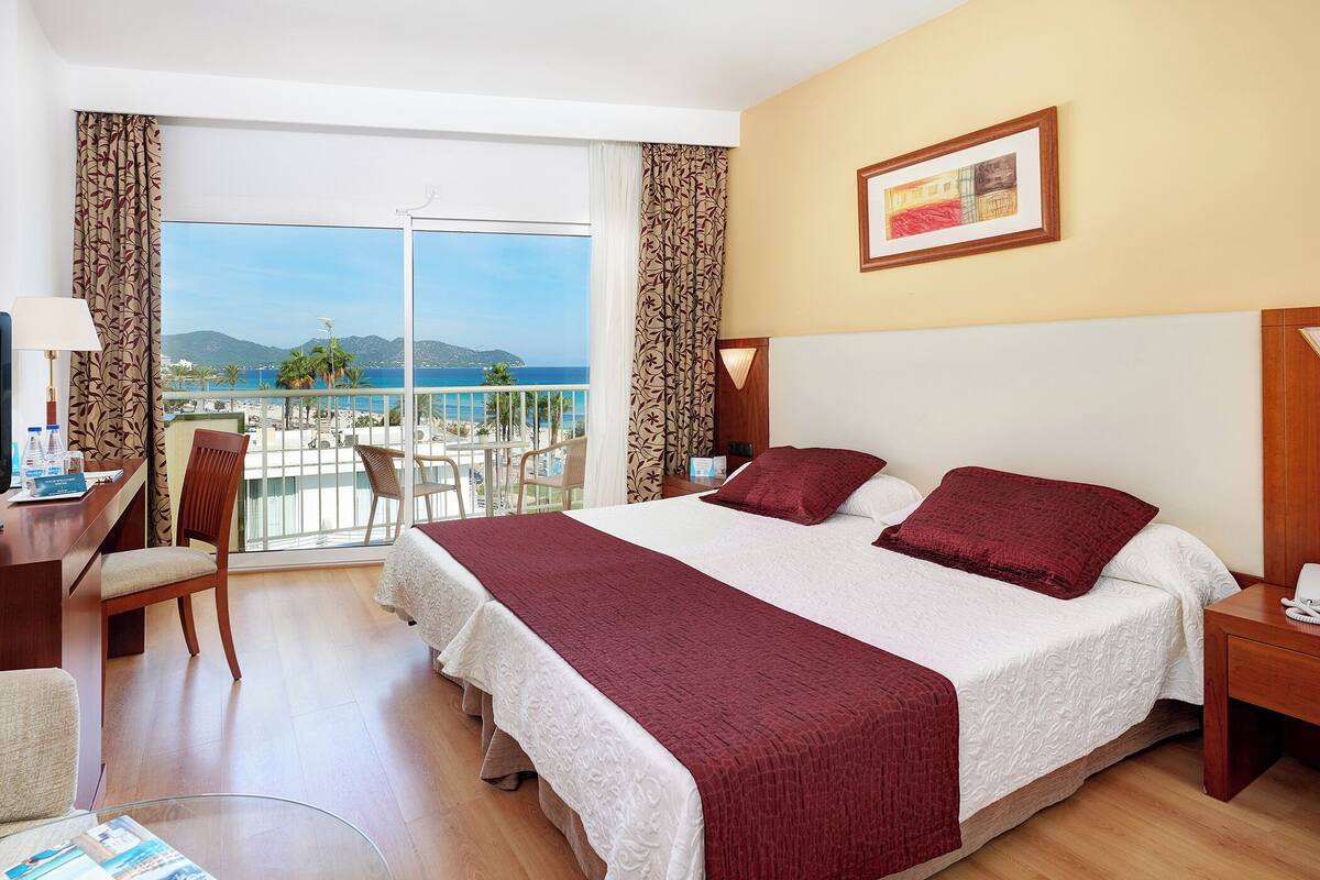 Ein Hotelzimmer mit Bett, Schreibtisch mit Fernseher, Stuhl und Blick auf den Strand.