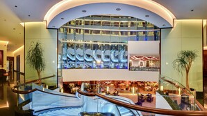 A modern hotel lobby with a glass atrium, multiple levels, and a central escalator. - Sofitel Al Khobar The Corniche (Al Khobar)