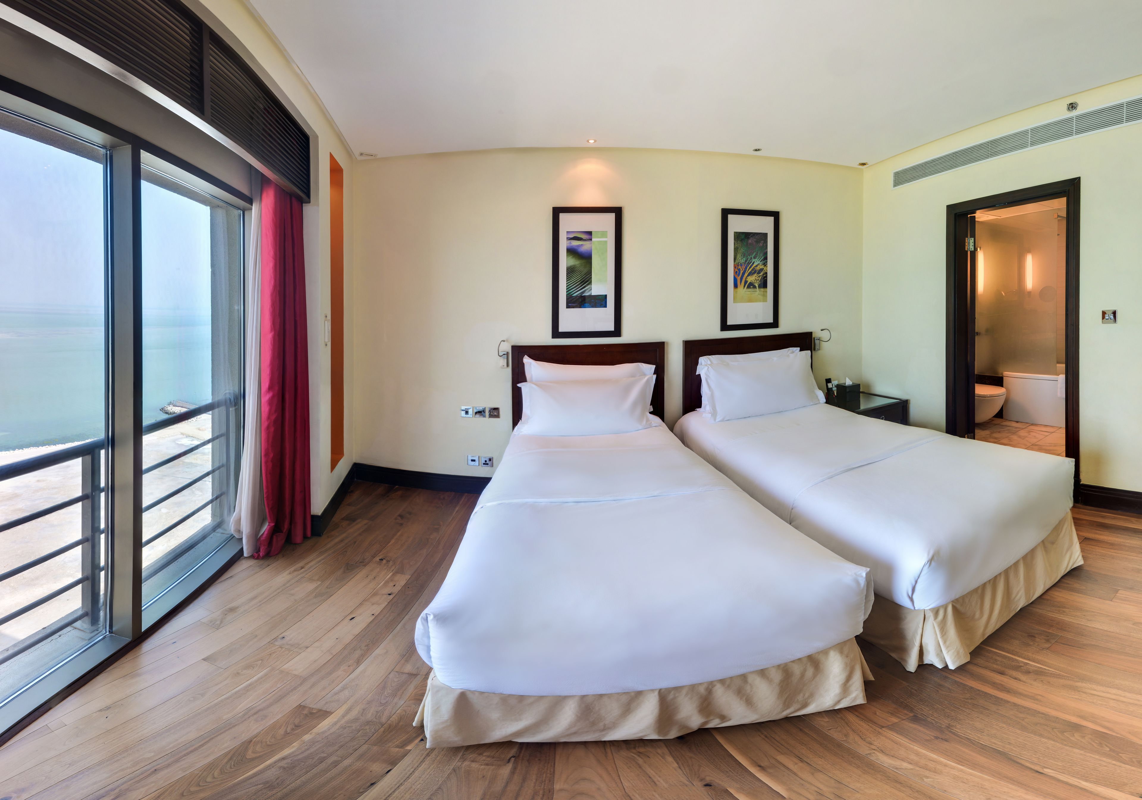 A hotel room with two beds, a large window with a view, and a door leading to a bathroom.