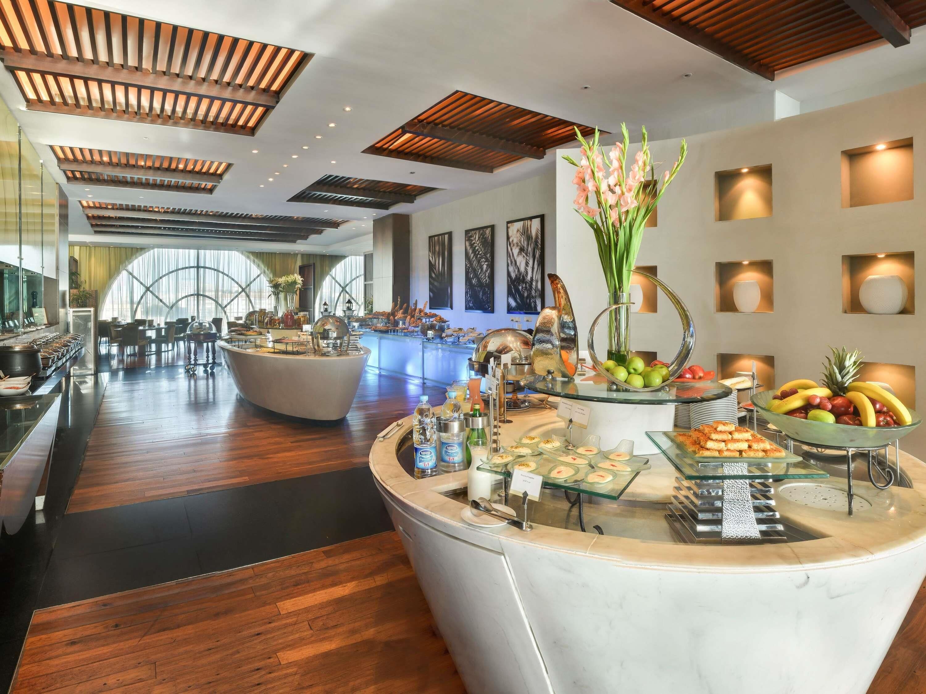 A modern hotel lobby with a central buffet area, wooden ceiling design, and large windows.
