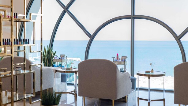 A modern interior with a large glass window offering a view of the sea. There are seating areas and a shelf with various items. - Sofitel Al Khobar The Corniche (Al Khobar)