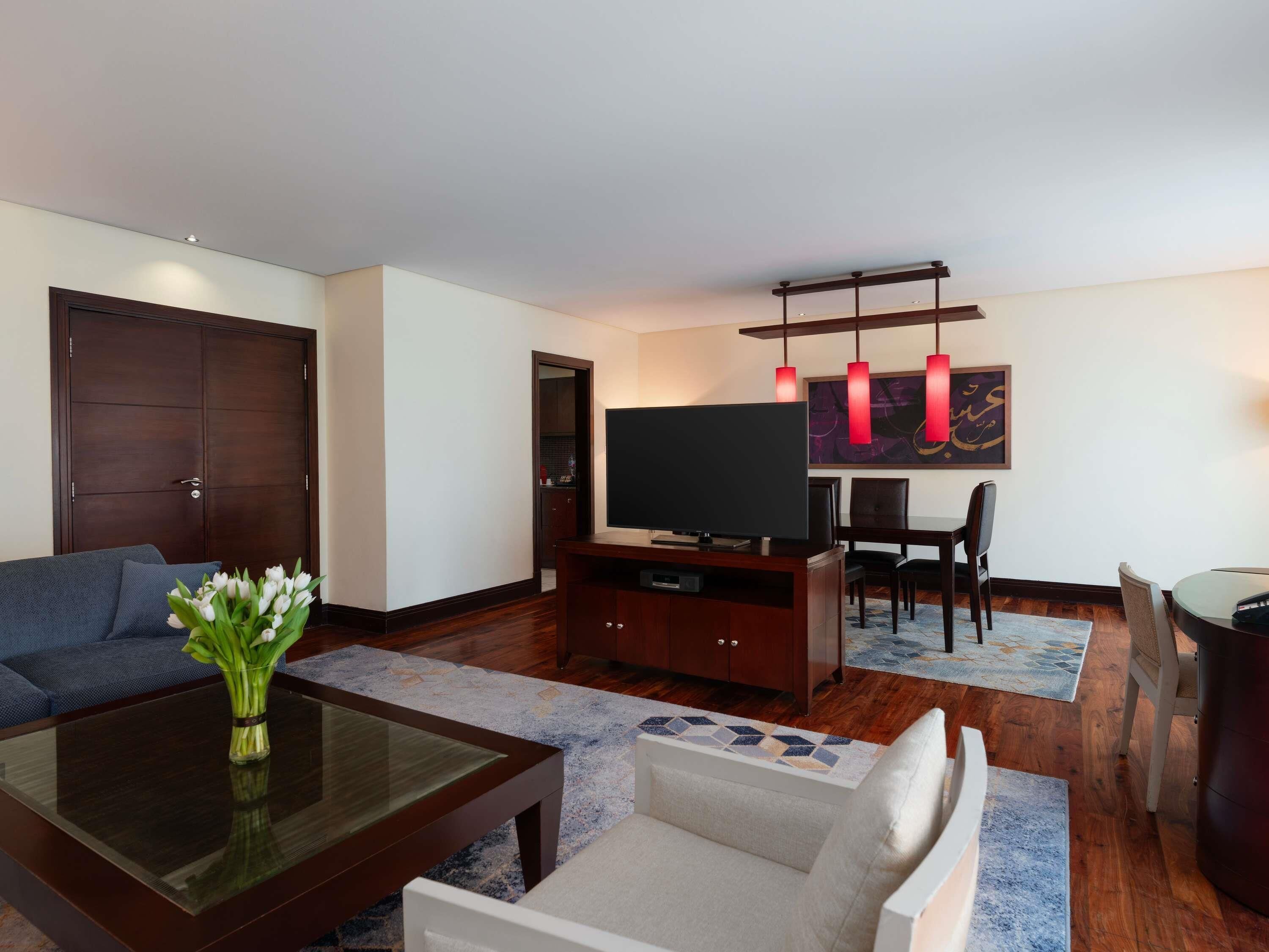 A modern living room with a sofa, a coffee table, a TV, and a dining area with chairs and a table.